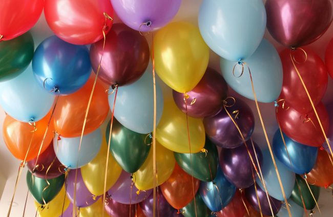 Colorful bright balloons filled with helium hang from the ceiling